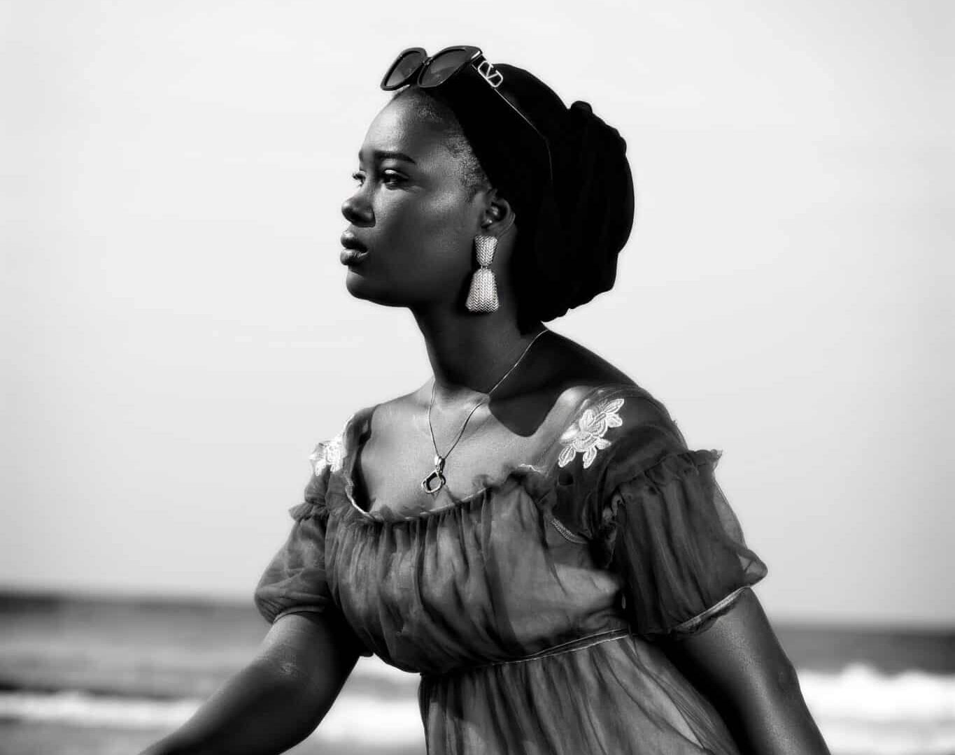 Black and white image of African female model Kira next to a boat at the seaside in Senegal.